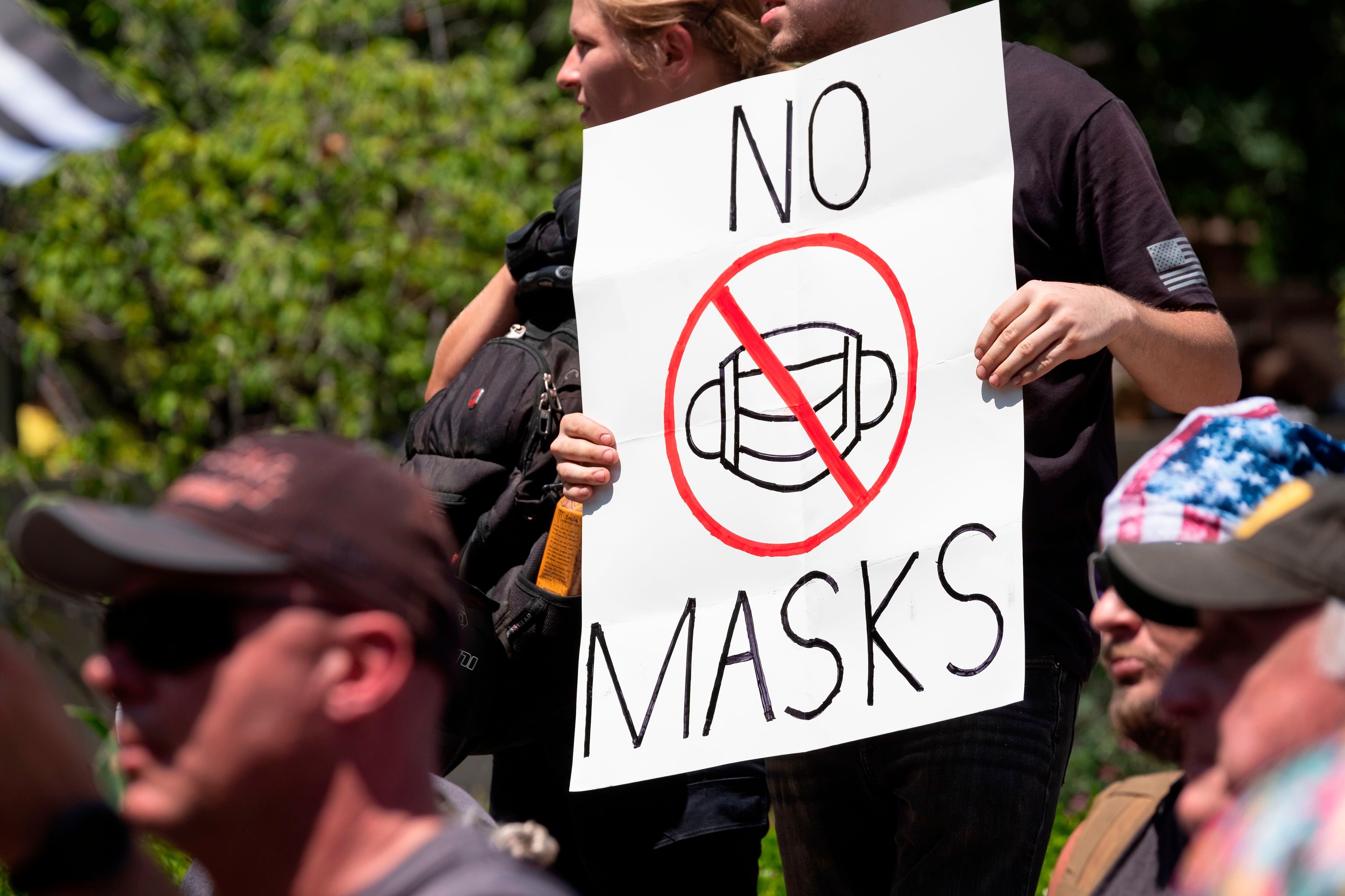 Un manifestant anti-masques brandit une pancarte en réponse aux lois locales exigeant que les...