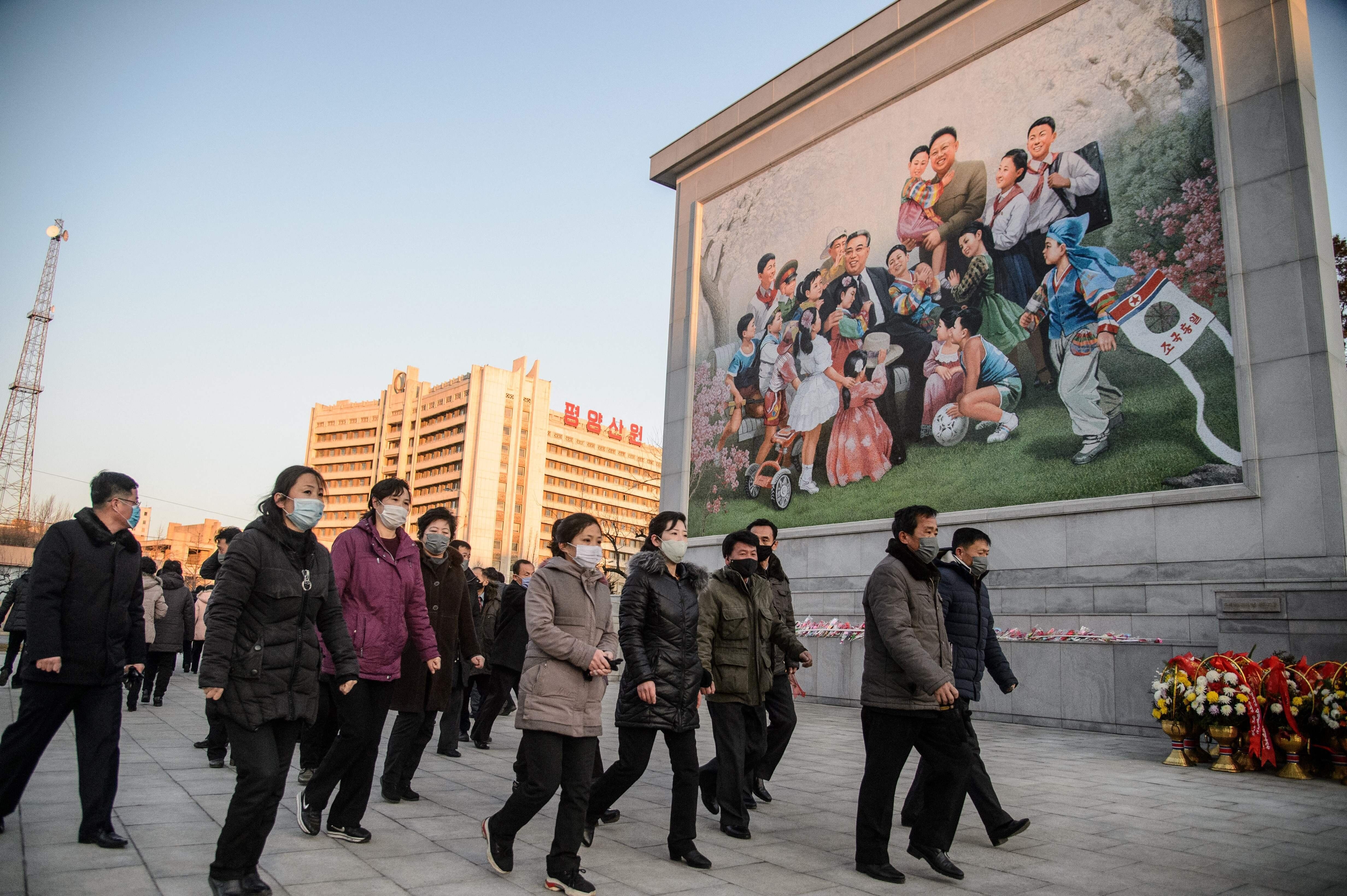Des personnes marchant devant une mosaïque représentant Kim Il Sung et Kim Jong Il, à...